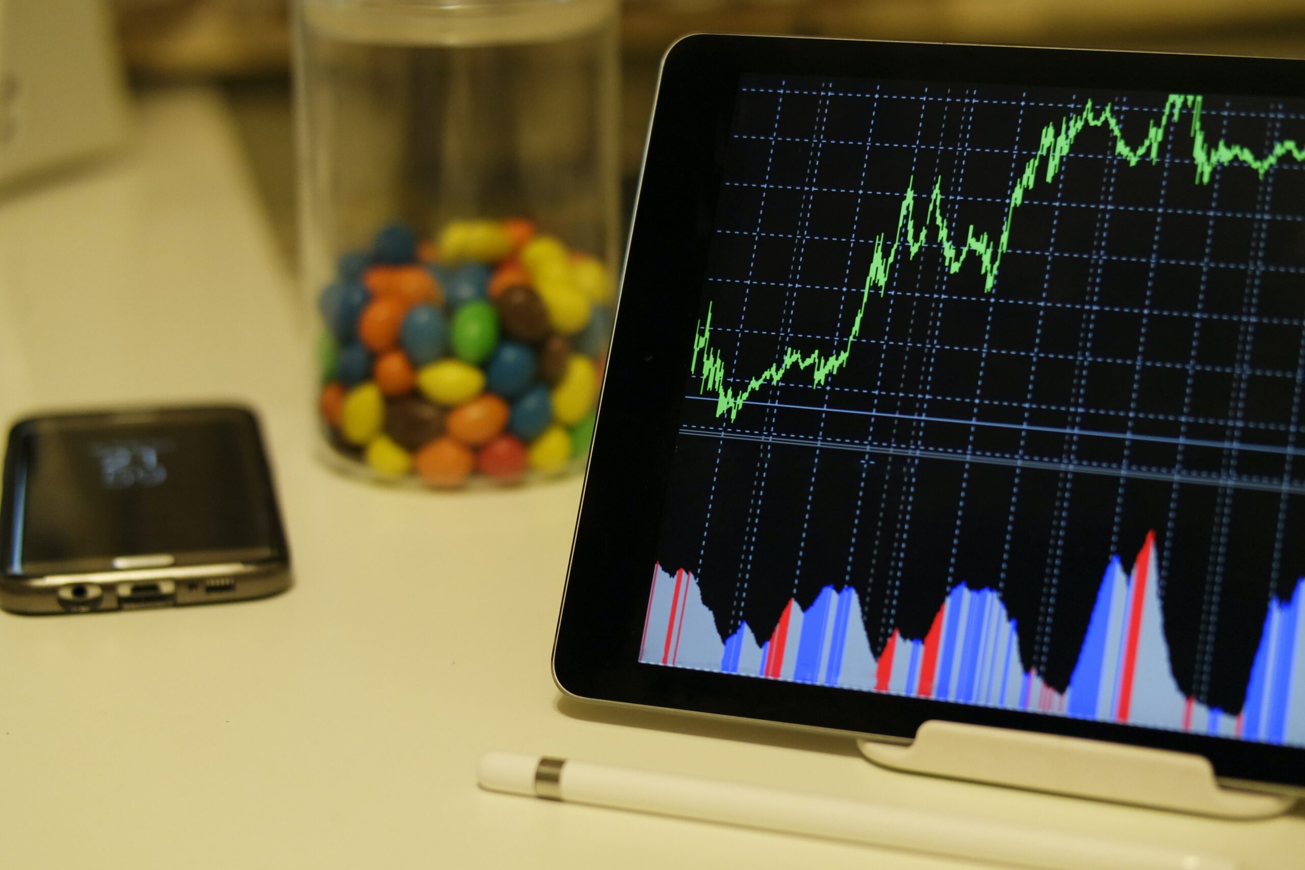 An image of a tablet that displays graphs and a line chart. A jar of candy and a cellphone are seen behind the tablet.